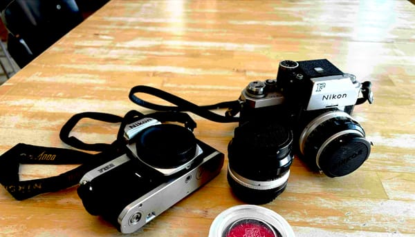 Film cameras and a lens on a wooden table, the analog tools of a writer exploring AI-assisted publishing.